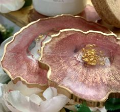 two pink and gold plates sitting on top of a wooden table next to white flowers