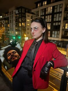 a woman in a red jacket and black tie is standing on a balcony at night