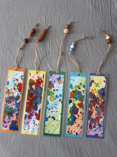 four colorful bookmarks are hanging from twine with string and beads on the end