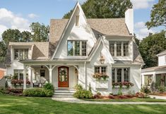 a white house with lots of windows and flowers in the front yard on a sunny day