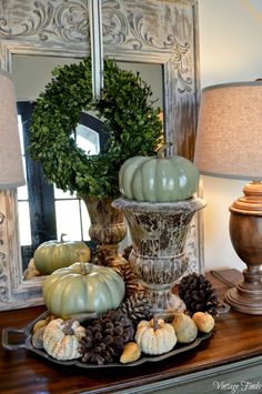 a table topped with green pumpkins and pine cones on top of a wooden table