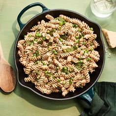 a skillet filled with pasta and peas on top of a green table next to a wooden spoon