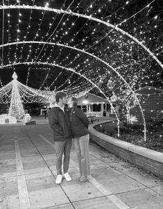 black and white photo of two people standing under an archway covered in christmas lights