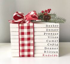 stack of christmas books wrapped in red and white checkered ribbon with pine cone on top