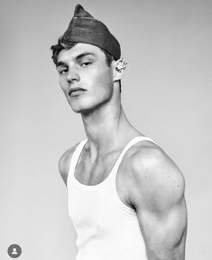 a young man in a tank top and hat poses for a black and white photo