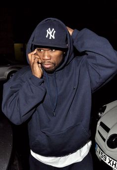 a man wearing a new york yankees hoodie talking on a cell phone while standing next to a car