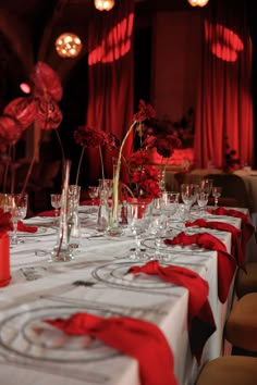 the table is set with wine glasses and red flowers in vases on each side