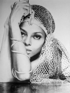 a black and white photo of a woman with her hands on her head, leaning against a table