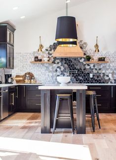 a kitchen with black cabinets and white tile backsplash, two stools in front of the island