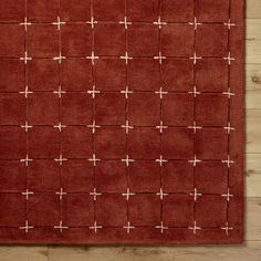 a red rug with white crosses on the top and bottom, sitting on a wooden floor