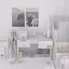 a white desk topped with lots of different types of office supplies and pictures on the wall