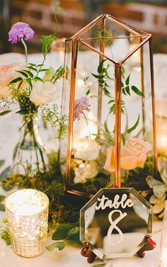 a table topped with candles and flowers next to a glass vase filled with greenery