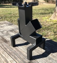 a black sculpture sitting on top of a wooden table in front of a tree and grass field