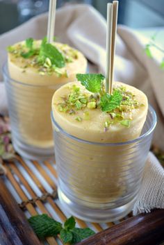 two glasses filled with dessert sitting on top of a wooden tray covered in green leaves