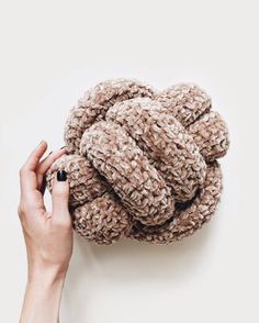 a hand holding a ball of yarn in front of a white wall