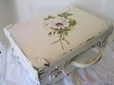 an old white suitcase with flowers painted on the lid and handles sitting on a table