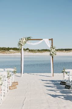 an outdoor ceremony set up with white chairs and flowers on the aisle, overlooking water