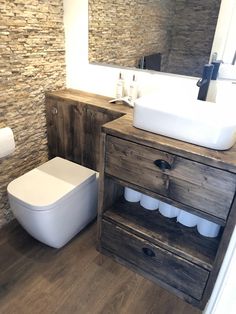 a white toilet sitting next to a wooden cabinet in a bathroom on top of a hard wood floor