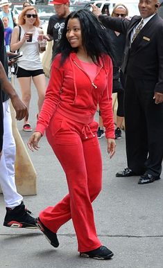 a woman in a red jumpsuit is walking on a skateboard and people are standing around