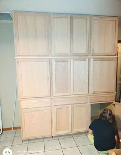 a woman kneeling on the floor in front of some cupboards with doors and drawers