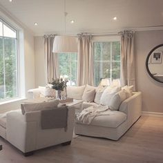 a living room filled with white furniture and large windows next to a wooden flooring area