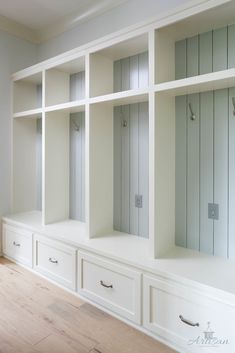 an empty room with white shelves and drawers on the wall, next to a wooden floor