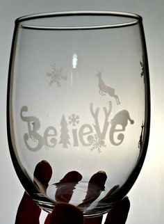 someone holding up a wine glass with the word believe etched in it's bottom