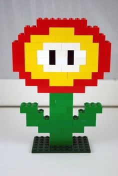 a lego model of a red flower with yellow petals and green leaves on it's base