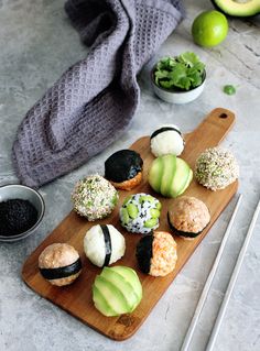 a wooden cutting board topped with different types of sushi and avocado on top of a table