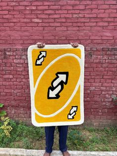 a person standing in front of a brick wall holding up a yellow and white sign