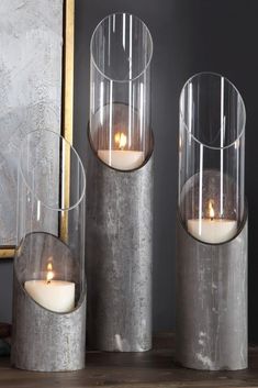 three candles are sitting in metal containers on a table next to a painting and books