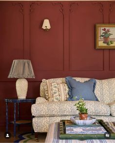 a living room filled with furniture and a lamp on top of a coffee table in front of a red wall