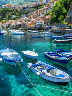 many small boats are docked in the clear blue water next to an island with houses on it