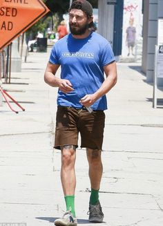 a man walking down the street in shorts and a blue t - shirt with green socks