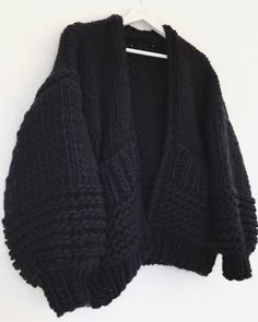 a black cardigan sweater hanging on a white hanger, with the top half open