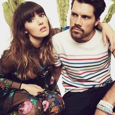 a man and woman sitting next to each other in front of cacti on the wall