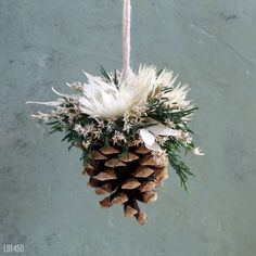 a pine cone ornament hanging from a rope with white flowers and greenery