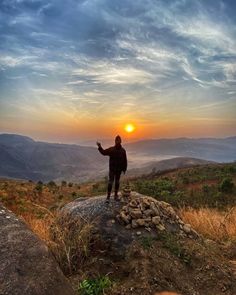 a man standing on top of a rock with the sun setting in the distance behind him