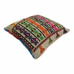 an embroidered pillow with multicolored geometric designs on the front and back, sitting on a white surface