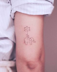 a small elephant tattoo on the left inner arm and shoulder, with a flower coming out of its trunk