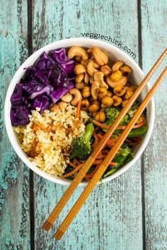 a white bowl filled with rice, broccoli and carrots next to chopsticks