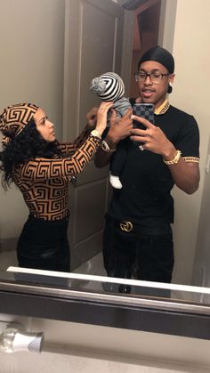 a man and woman standing in front of a bathroom mirror holding a baby girl up to her face