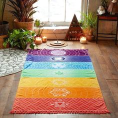 a rainbow rug in the middle of a room with potted plants and candles on the floor