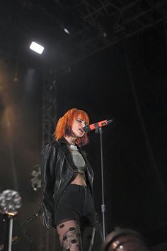 a woman with red hair and tattoos on her leg standing in front of a microphone