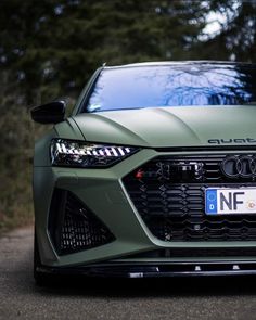 the front end of a green sports car on a road with trees in the background