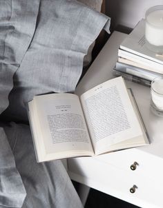 an open book sitting on top of a white table next to a cup and candle