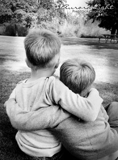 two young boys sitting on the ground hugging each other