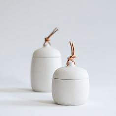 two white ceramic containers with twine on the top one has a brown string attached to it