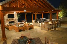 an outdoor kitchen and dining area with wood beams on the ceiling, lighting up the patio at night