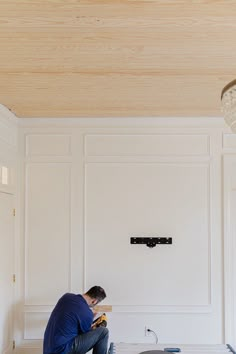 a man kneeling down on the floor in front of a white wall with wood paneling